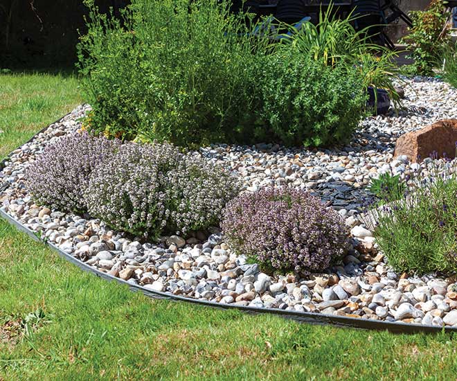 Un parterre de fleurs et de plantes avec des cailloux en guise de paillage et un contour pour délimiter le parterre de la pelouse dans un jardin de l'Oise.