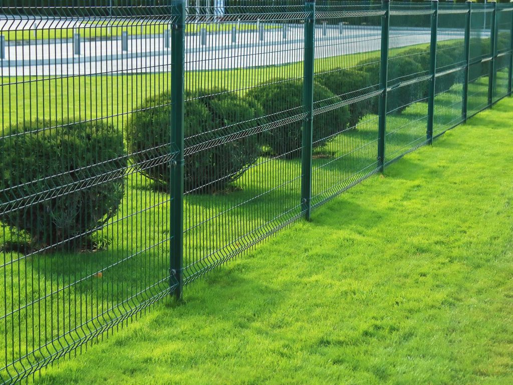 une clôture de panneau rigides de type treillis soudés de couleur vert foncées arbustes taillés en boule en arrière et une pelouse verte très belle dans l'Oise